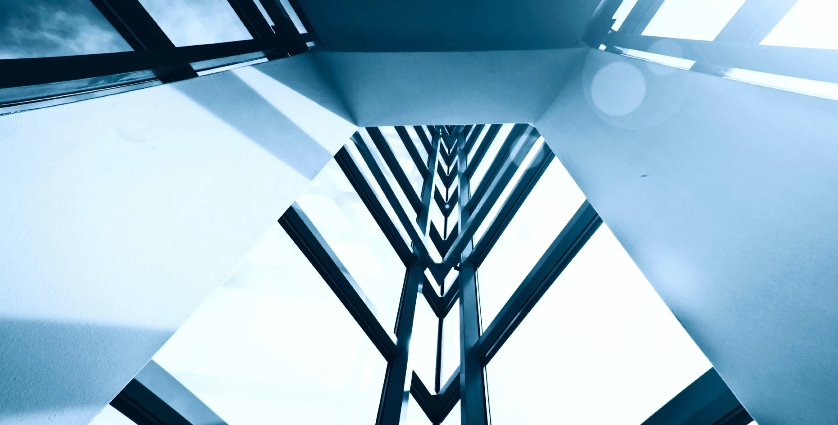 Abstract upward view of a modern building's glass and steel framework with clean white walls and sunlight filtering through.