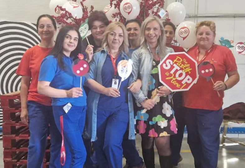 Group of eight women posing indoors, holding balloons and signs including a red stop sign reading 'The Party STOP is Here!'
