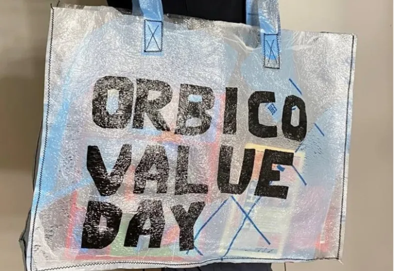 A translucent shopping bag with blue handles and black text reading 'ORBICO VALUE DAY' printed on it.