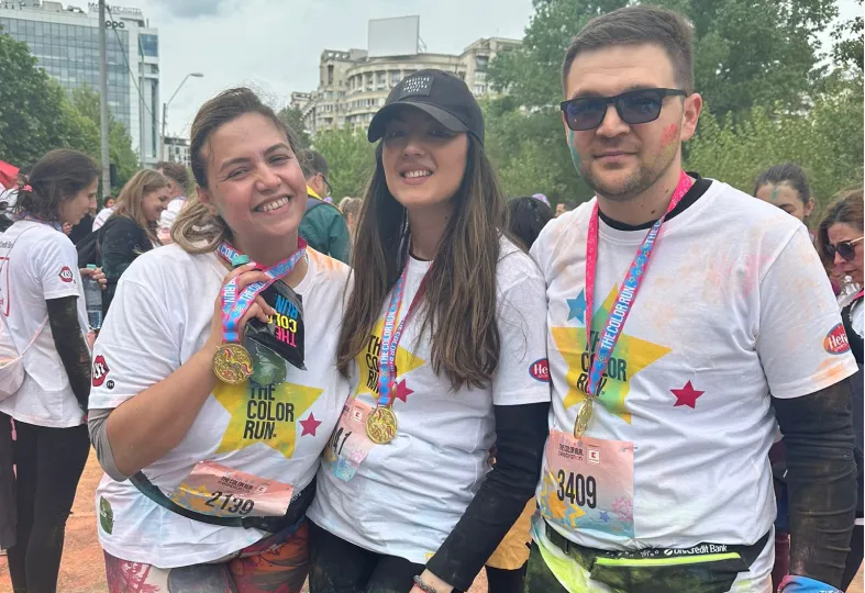 Three smiling participants wearing The Color Run shirts and medals at an outdoor event.