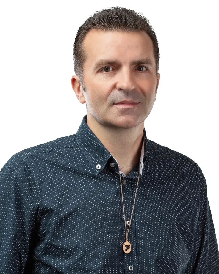 Man with short dark hair wearing a dark blue polka dot shirt and a wooden pendant necklace with a bird silhouette.