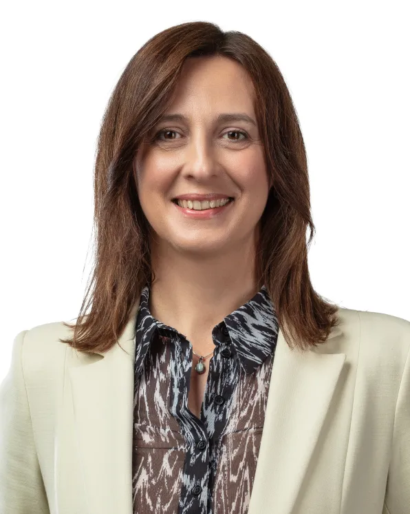 Smiling woman with shoulder-length brown hair wearing a patterned blouse and light-colored blazer against a white background.