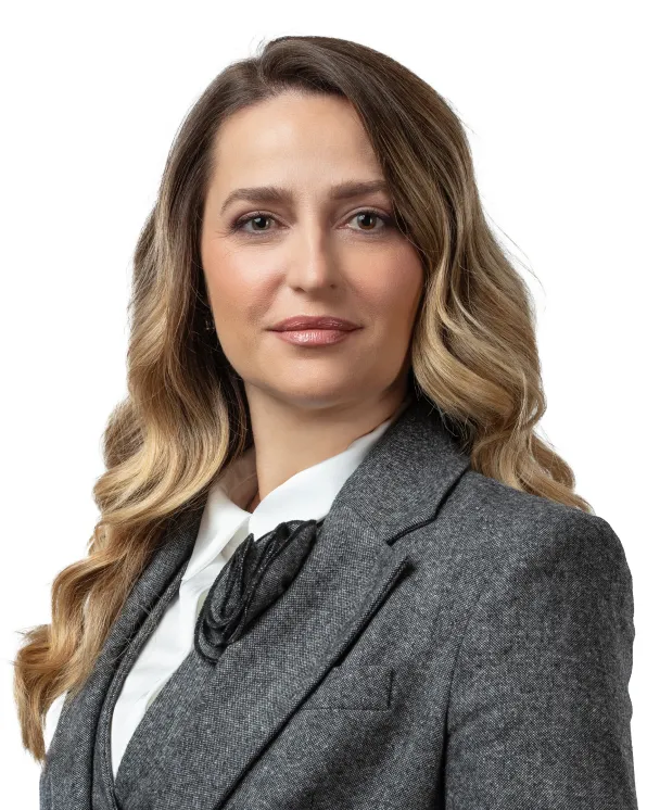 Professional woman with long wavy blonde hair wearing a gray blazer and white blouse, looking confidently at the camera.