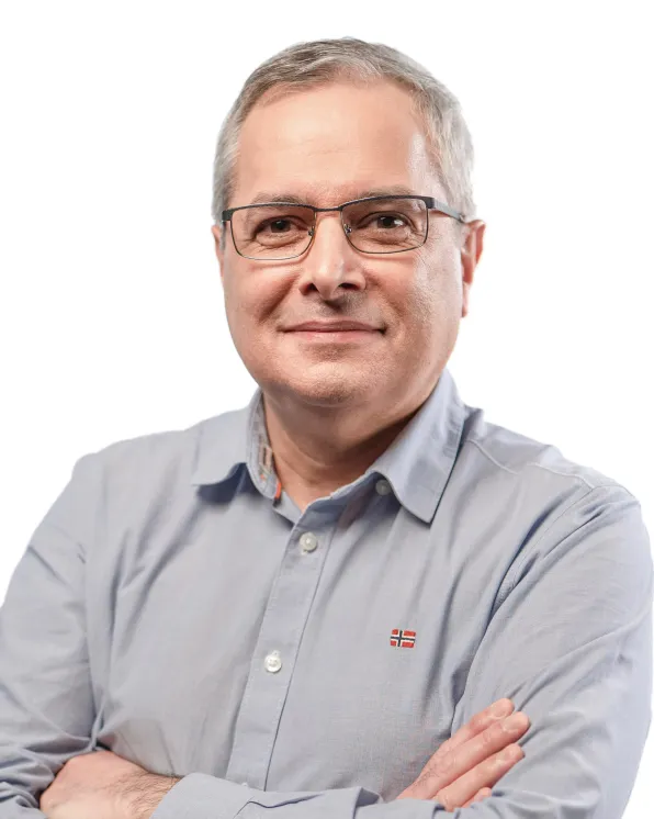 Middle-aged man with glasses wearing a light blue button-up shirt with arms crossed, smiling subtly against a white background.