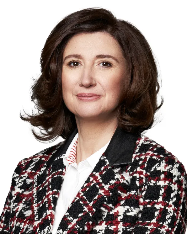 Woman with shoulder-length brown hair wearing a black, white, and red patterned jacket over a white shirt, smiling slightly against a white background.