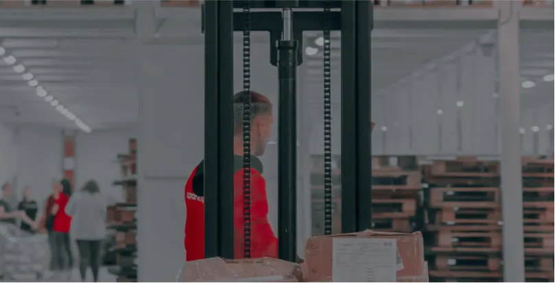 Warehouse worker operating a forklift to move wrapped pallets in an industrial storage area.