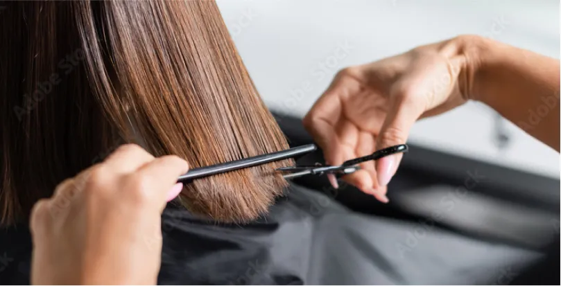 Close-up of a hairstylist cutting straight brown hair with scissors and a comb.