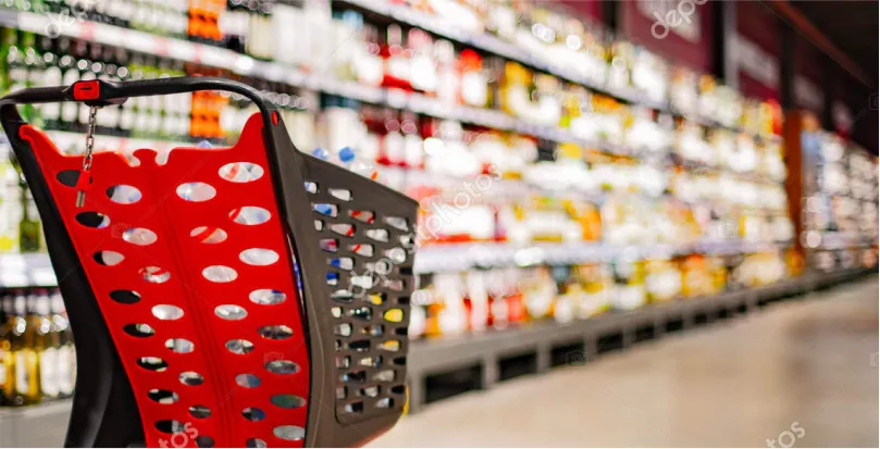 Red and black shopping cart in an aisle of a grocery store with blurred shelves of bottles and products in the background.