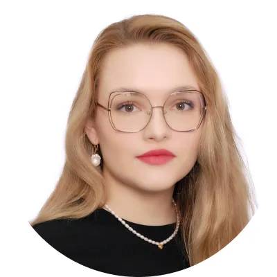 Portrait of a woman with long blonde hair wearing large square glasses, pearl necklace, and black top.