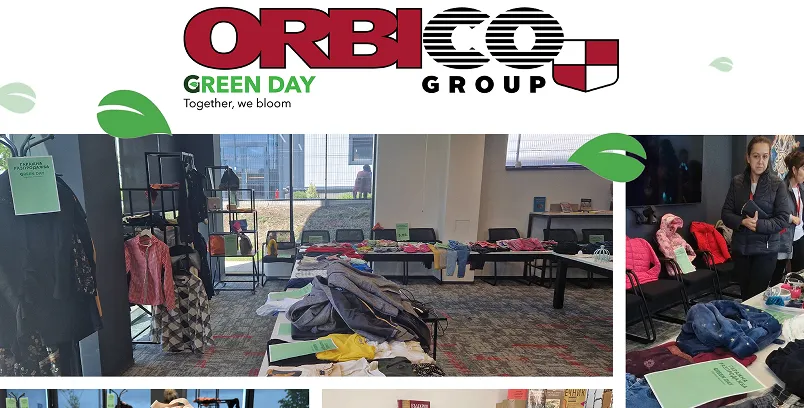 Indoor room with tables displaying folded clothes, racks with hanging garments, and two people standing nearby, part of Orbico Group Green Day event.