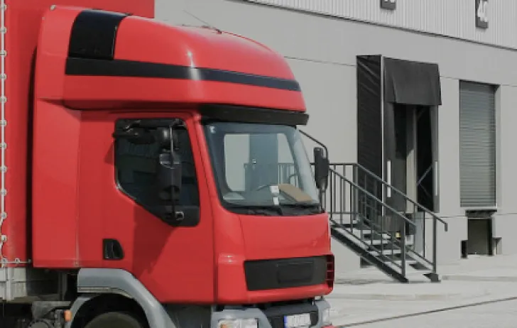 Close-up of a red semi-truck cab parked beside an industrial building with loading dock stairs and closed shutters.